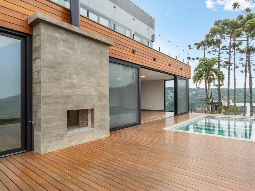 Deck de madeira com piscina, portas de correr escuras de piso a teto e araucárias ao fundo
